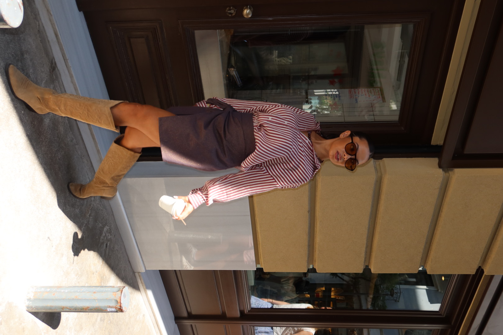 Woman in a striped shirt, dark skirt, and cowboy boots walking on a city street