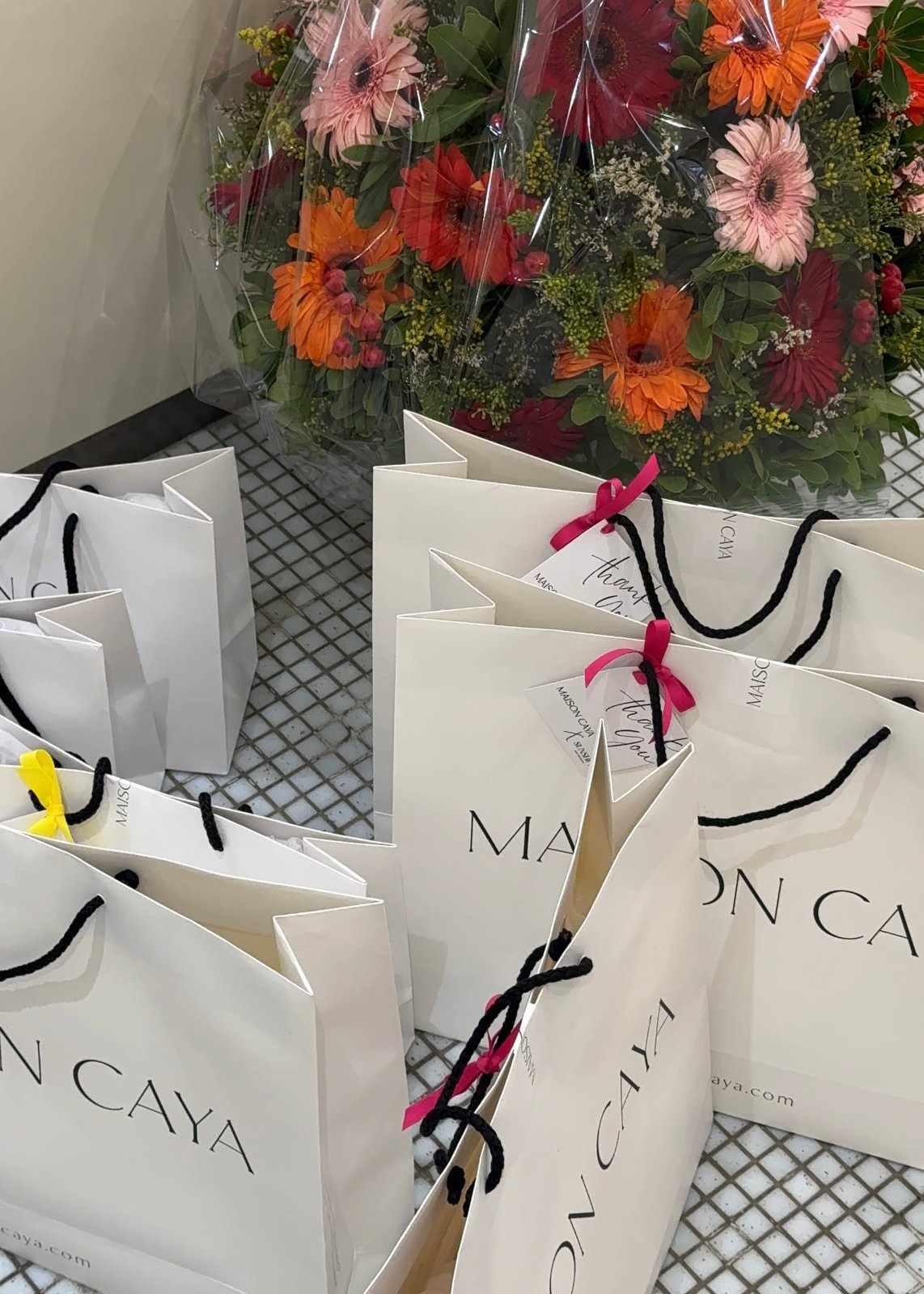 White Maison Caya gift bags beside bouquets of gerbera flowers