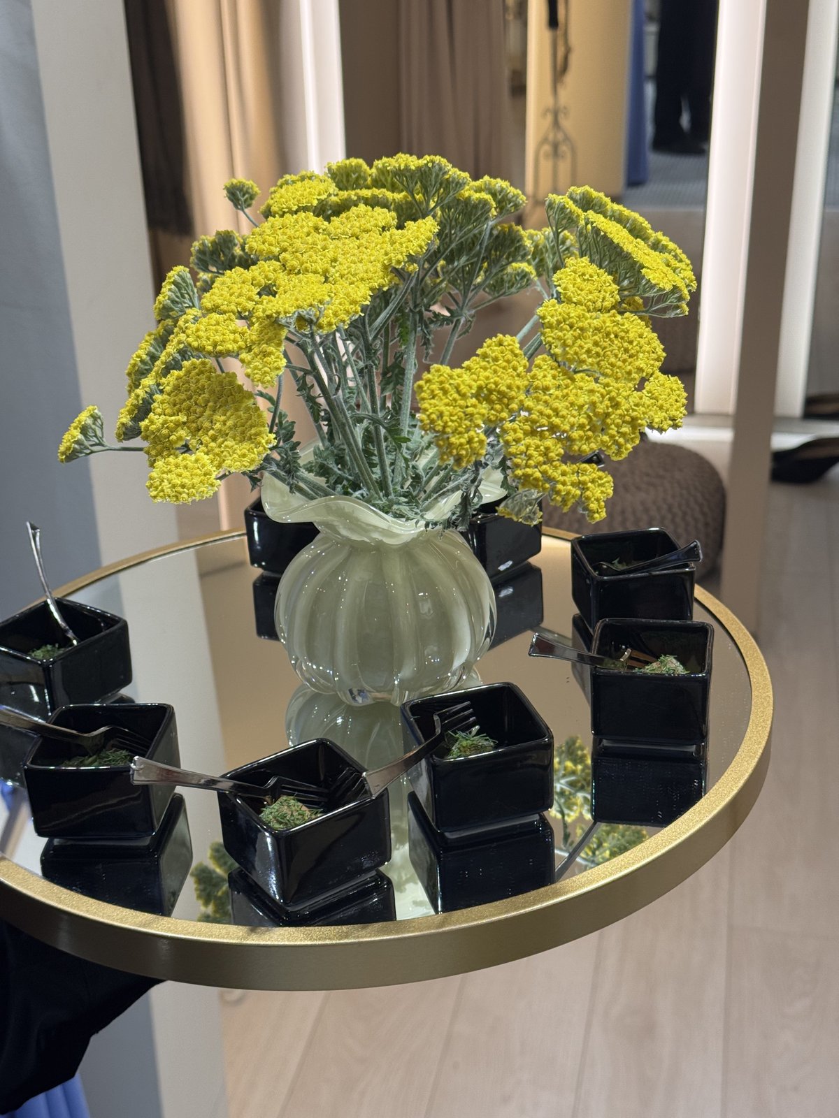 Yellow flowers in a glass vase on a mirrored tray with black condiment bowls